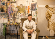 P Addy Critchley sitting in his painting studio in white overalls with large paintings behind him
