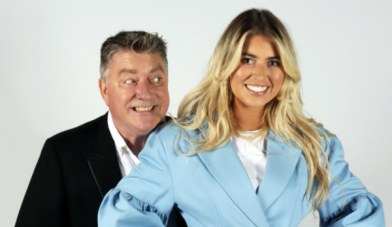 Image features Pat Shortt smiling at Faye Shortt who is dressed in a blue suit and they are standing in front of a bright white background