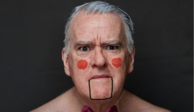 Close up portrait of actor and thatremaker mikel murfi wearing a dicky bow and with rouged cheeks and a lined mouth that gives him the appearance of a puppet