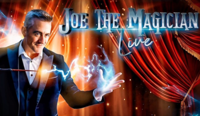 Joe the magician with blue sparks coming from his wand into his other hand on a stage with red curtains