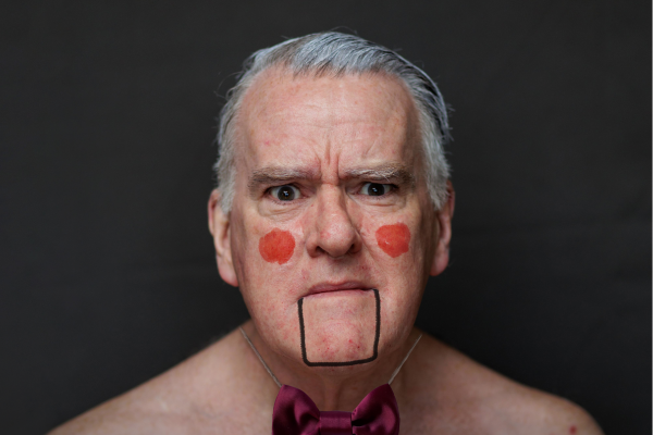 Close up portrait of actor and thatremaker mikel murfi wearing a dicky bow and with rouged cheeks and a lined mouth that gives him the appearance of a puppet