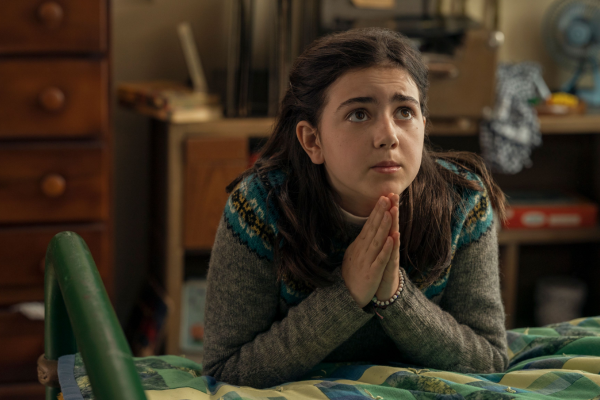 Image of young girl with dark hair praying by her bed