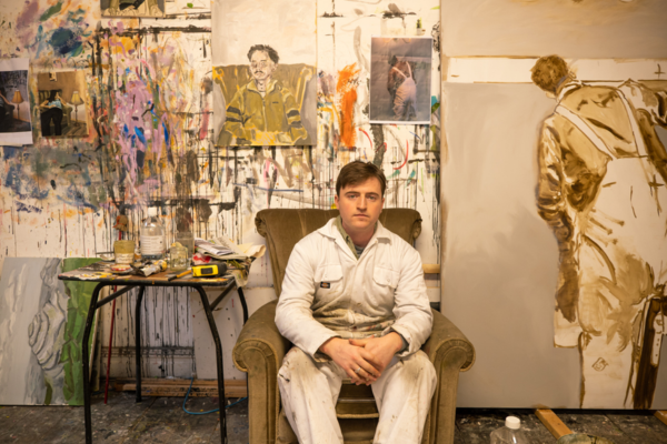 P Addy Critchley sitting in his painting studio in white overalls with large paintings behind him