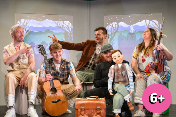4 people on stage one holds a puppet and 2 hold instruments having fun and laughing together