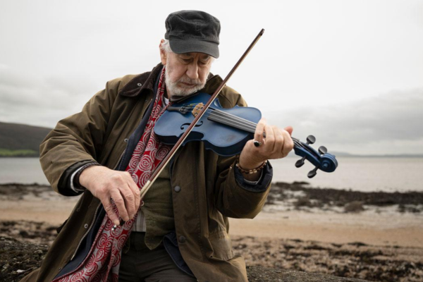 An older man plays the fiddle on a beach as the image for the irish film fidil ghorm