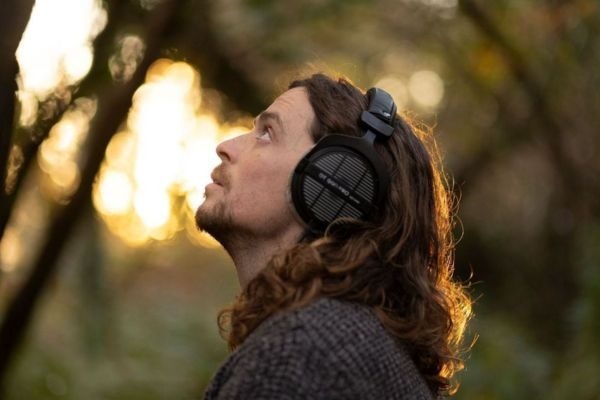 Man with headphones looking up with trees and sunshine behind him